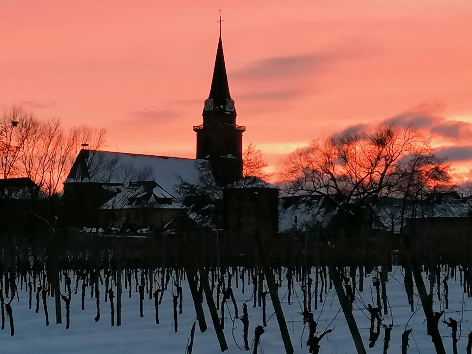 Le clocher se découpe sur un ciel rouge d’hiver